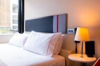 a bed with white pillows and a lamp next to a window at citizenM Southwark Bankside in London
