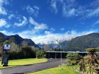 una carretera que conduce a un edificio con montañas en el fondo en Sunset Motel, en Fox Glacier