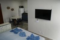 a living room with a television and a bed with blue sheets at Flat Sirena - São Vicente in São Vicente
