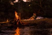 Dos personas sentadas alrededor de una fogata junto a un río. en Athgira River Camping - Udawalawe, en Udawalawe