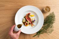 una persona sosteniendo un plato blanco con comida sobre una mesa en Althoff Hotel Villa Belrose, en Saint-Tropez