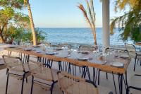 Zanziblue Waves Beach Resort في كيوينجوا: طاولة خشبية طويلة مع الكراسي والمحيط