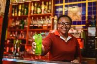 Un hombre parado detrás de una barra sosteniendo una bebida verde. en Hotel Chalet des Roses, en Antananarivo