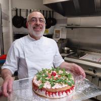 Un hombre de pie en una cocina sosteniendo un pastel. en Hotel Paris Vesinet-LogisHotels et Domaine Evenementiel, en Le Vésinet