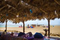 una playa con sombrilla de paja y gente en la playa en Green Sudr Kitesurfing Hotel, en Raʼs Matarma