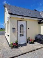 un pequeño edificio blanco con una puerta y flores en Doolin Farm Apartment, en Doolin