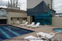 a swimming pool with white chairs and a building at Flat Sirena - São Vicente in São Vicente