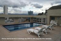 a swimming pool with white chairs on a building at Flat Sirena - São Vicente in São Vicente
