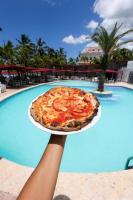 a person holding a pizza on a plate in front of a pool at Boca Beach Residence hotel in Boca Chica