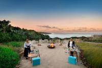 two women are sitting around a table with a fire at GweGwe Beach Lodge in Mkambati