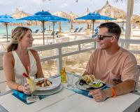 a man and a woman sitting at a table eating food at the beach at Amsterdam Manor Beach Resort in Palm-Eagle Beach