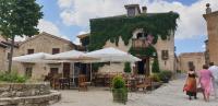 personas caminando frente a un edificio con mesas y sombrillas en El Refugio de Pedraza, en Pedraza-Segovia