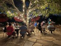 un groupe de personnes assises à des tables sous un arbre dans l'établissement Medina River Oaks Courts, à Medina