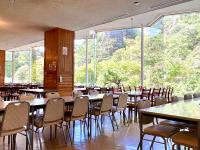a dining room with tables and chairs and large windows at 国民宿舎古岩屋荘 in Higashi-komi