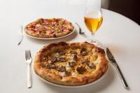 two pizzas sitting on a table with a glass of beer at Impression Isla Mujeres by Secrets - Adults Only - All Inclusive in Isla Mujeres