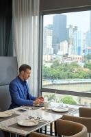 un hombre sentado en una mesa frente a una ventana en MADR Excellence at Novotel Manila Hotel Residence Acqua, en Manila