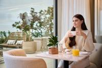 una mujer sentada en una mesa con una taza de café en Hotel Petit Bois - Adults from 14, en Balatonfüred