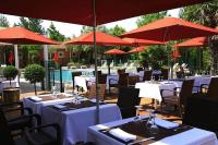 a restaurant with white tables and red umbrellas at SOWELL HOTELS Domaine de la Petite Isle in LʼIsle-sur-la-Sorgue