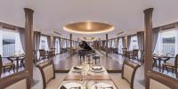 Paradise Legacy Cruise Halong في ها لونغ: غرفة طعام مع طاولات وكراسي ونوافذ
