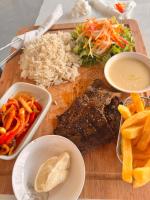 Una tabla de cortar de madera con arroz, carne y verduras. en MERAKI BEACH RESORT Lodges, en Lomé