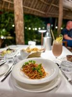 a plate of spaghetti on a table with a drink at Alma Boutique Hotel in Jambiani