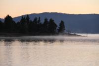 a misty lake with trees and a mountain in the background at Acacia Snowy Motel in Jindabyne