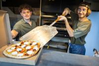 Dos hombres están haciendo una pizza en un horno. en Huttopia Beaulieu sur Dordogne, en Beaulieu-sur-Dordogne