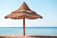 a straw umbrella on a sandy beach near the ocean at Herods Palace Hotels & Spa Eilat a Premium collection by Fattal Hotels in Eilat