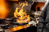 a person cooking food in a pan on a stove with flames at Renaissance Dallas Hotel in Dallas