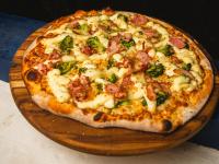 a pizza with broccoli and cheese on a wooden board at VELINN Pousada Bromelias in Ilhabela