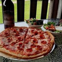 a pizza on a table with a bottle of beer and salad at Deer Creek Winery at Watson Estate in Uniontown