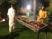 dos hombres parados junto a una parrilla con comida. en Mountain View Resort, en Islamabad