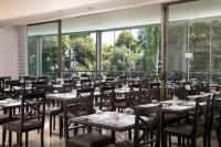 Un comedor con mesas y sillas y grandes ventanales. en Corfu Holiday Palace, en Corfú