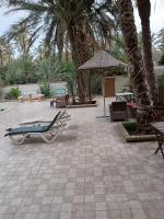 a patio with chairs and an umbrella and palm trees at Résidence Loued in Tozeur