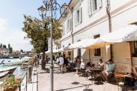 a group of people sitting at tables and umbrellas near a canal at Pavillon Apartments in Peschiera del Garda