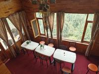 a room with two tables and chairs and windows at Apple Garden Cottage in Manāli