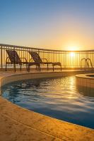 Dos bancos sentados junto a una piscina al atardecer en Green Hotéis, en Cabo Frío