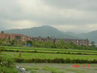a large field with buildings and mountains in the background at Relax heart B&amp;B in Dongshan