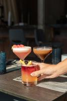 una persona sosteniendo dos cócteles en una mesa en The LOOM Hotel, Tapestry Collection by Hilton, en Warwick
