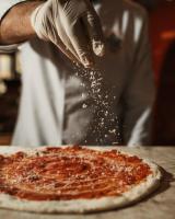 una persona espolvoreando pepperoni encima de una pizza en Hotel Alta Garrotxa, en Tortellà
