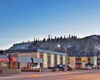 a building with a mountain in the background with cars parked at Quality Inn &amp; Suites in Whitehorse