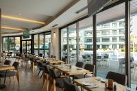 Un restaurante con mesas y sillas de madera y ventanas. en Helena Sea Breeze Apartments - Resort Living with Pools & Full Facilities, en Rizokarpaso