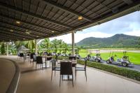 a restaurant with tables and chairs and golf carts in the background at Tinidee Golf Resort Phuket in Kathu