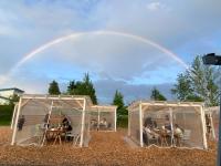 een regenboog boven twee koepels met mensen die aan tafels zitten bij Glamp Sora Furano in Nakafurano
