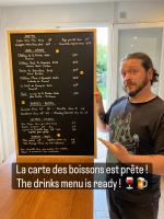 een man staat naast een schoolbord met een menukaart bij Amis Wine House in Pomerol