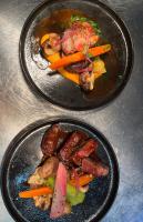 Dos platos negros de comida con carne y verduras. en Logis Hotel Spa Restaurant Au Site Normand, en Clécy