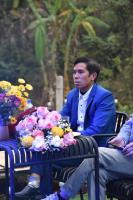 枚州县Mai Châu Medifarm Retreat的一位身穿西装的男士坐在长椅上，身边摆放着鲜花。