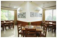 um restaurante com mesas e cadeiras de madeira e janelas em Arogyadham Swasthya Kutir em Chitrakoot