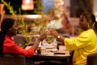 dwie kobiety siedzące przy stole i pijące napoje w obiekcie Inyoni Boutique Hotel and Restaurant w mieście Gisenyi