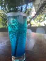 un verre de liquide bleu posé sur une table en bois dans l'établissement The Twins Sunset Bungalow, à Palebah